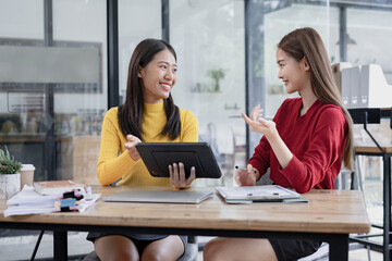 Two Asian businesswomen discussing work a digital tablet setting in a modern office, 