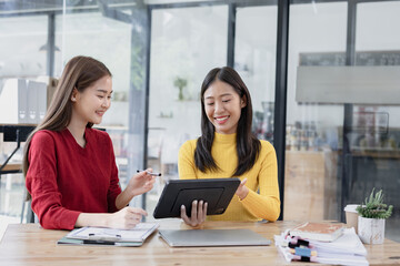 Two Asian businesswomen discussing work a digital tablet setting in a modern office, 