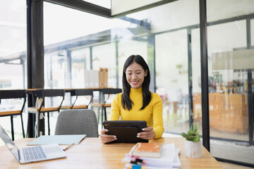 Happy young Asian businesswoman using digital tablet sitting in office.