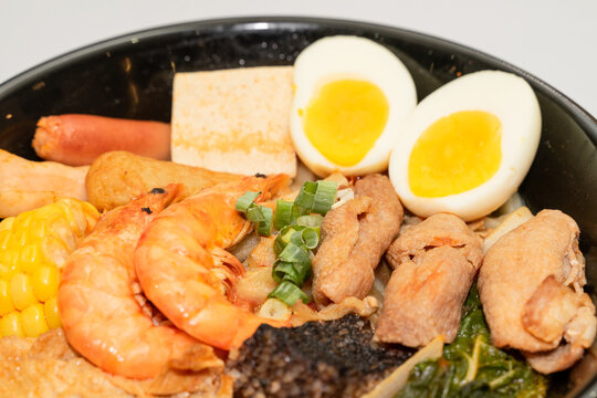 A hearty bowl of seafood noodle soup filled with shrimp, corn, egg, vegetables, rice blood cake, tofu skin, and assorted hotpot ingredients. The colorful ingredients float in a rich broth, making for 