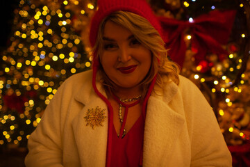 Plus size woman walks around the city during the Christmas of the week with a hot drink in a glass against the background of flickering light bulbs