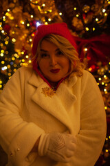 Plus size woman walks around the city during the Christmas of the week with a hot drink in a glass against the background of flickering light bulbs