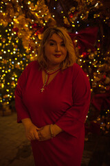 Plus size woman walks around the city during the Christmas of the week with a hot drink in a glass against the background of flickering light bulbs