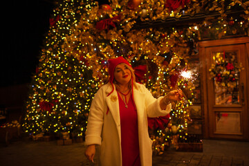 Plus size woman walks around the city during the Christmas of the week with a hot drink in a glass against the background of flickering light bulbs