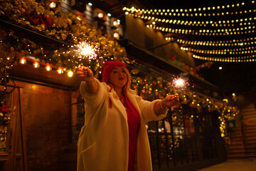 Plus size woman walks around the city during the Christmas of the week with a hot drink in a glass against the background of flickering light bulbs