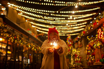 Plus size woman walks around the city during the Christmas of the week with a hot drink in a glass against the background of flickering light bulbs