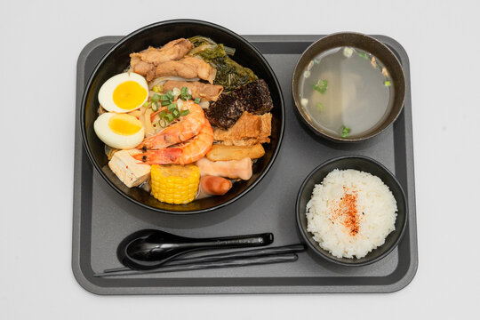 A hearty bowl of seafood noodle soup filled with shrimp, corn, egg, vegetables, rice blood cake, tofu skin, and assorted hotpot ingredients. The colorful ingredients float in a rich broth, making for 