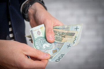 Elegant man counting Polish 100 zloty banknotes. Wealth, finance, and personal success concept. Close-up of male hands holding money in formal setting
