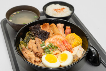 A hearty bowl of seafood noodle soup filled with shrimp, corn, egg, vegetables, rice blood cake, tofu skin, and assorted hotpot ingredients. The colorful ingredients float in a rich broth, making for 