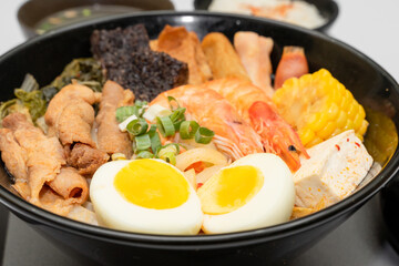 A hearty bowl of seafood noodle soup filled with shrimp, corn, egg, vegetables, rice blood cake,...
