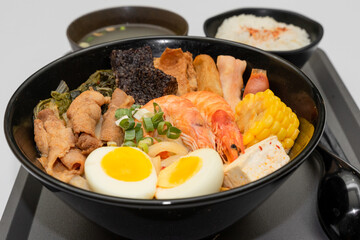 A hearty bowl of seafood noodle soup filled with shrimp, corn, egg, vegetables, rice blood cake, tofu skin, and assorted hotpot ingredients. The colorful ingredients float in a rich broth, making for 