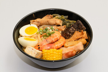 A hearty bowl of seafood noodle soup filled with shrimp, corn, egg, vegetables, rice blood cake,...