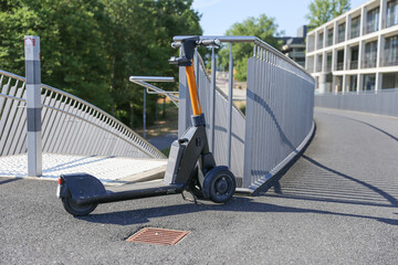 A parked scooter stands alone by the sidewalk next to a bridge – a calm, urban scene.