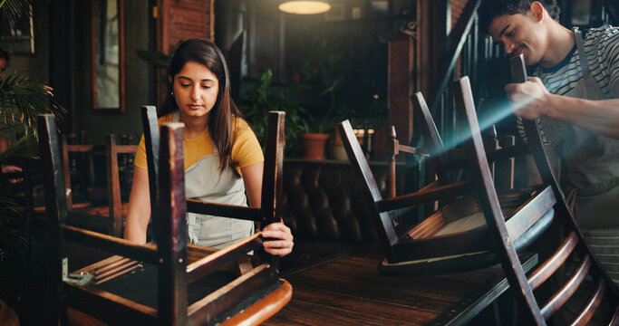 People, waiter and arranging chairs at cafe for closing time, cleaning routine and space management. Man, waitress and teamwork for layout, reserved seating and out of service of hospitality industry
