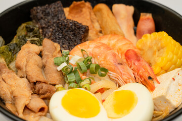 A hearty bowl of seafood noodle soup filled with shrimp, corn, egg, vegetables, rice blood cake,...