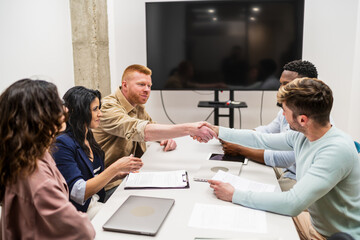 Coworkers shaking hands after reaching an agreement during a business meeting in a modern coworking...