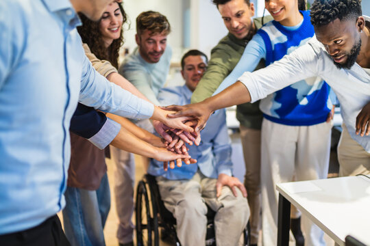 Coworkers stacking hands, showing unity and teamwork in a modern office environment, celebrating a shared goal or achievement