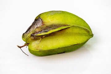 A whole green star fruit (Averrhoa carambola) on a white background, showing early signs of decay. Visible evidence of the fruit beginning to rot.