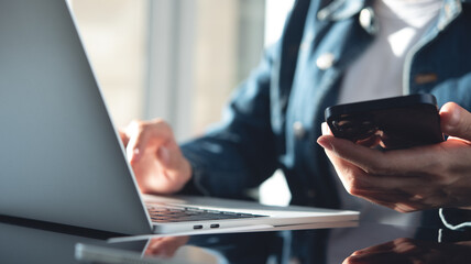Closeup, business woman sitting at table using mobile  phone during working on laptop computer at...
