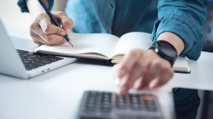 Doing finance, budgeting and tax calculation. Close up woman hand using calculator to calculate home finance, accounting with laptop computer on table, budget management, monthly expenses.