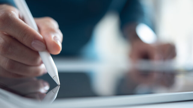 Close up, business woman hand using stylus pen signing on digital tablet via mobile app on office table. Graphic designer working on graphic tablet, drawing by using electronic pen
