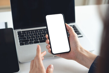 Blank white screen cell phone mockup. Close up, woman using smartphone on office table during working on laptop computer and digital tablet, empty space for social media marketing or mobile app design