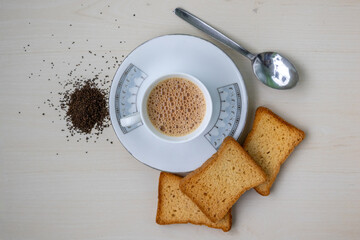 Hot frothy milk tea in teacup with crispy rusk biscuits. Fresh and dried tea leaves on wooden...