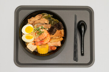 A hearty bowl of seafood noodle soup filled with shrimp, corn, egg, vegetables, rice blood cake, tofu skin, and assorted hotpot ingredients. The colorful ingredients float in a rich broth, making for 