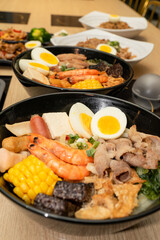 A hearty bowl of seafood noodle soup filled with shrimp, corn, egg, vegetables, rice blood cake, tofu skin, and assorted hotpot ingredients. The colorful ingredients float in a rich broth, making for 