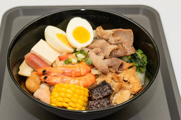 A hearty bowl of seafood noodle soup filled with shrimp, corn, egg, vegetables, rice blood cake, tofu skin, and assorted hotpot ingredients. The colorful ingredients float in a rich broth, making for 