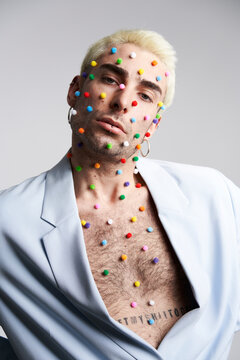 Trendy young man with multicolored pellets on face and neck looking at camera against gray background