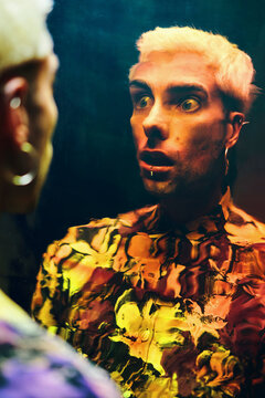 Astonished young guy with opened mouth looking at distorted reflection on dichroic film