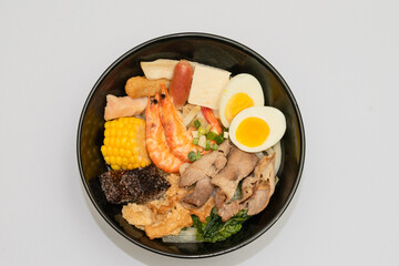 Fototapeta premium A hearty bowl of seafood noodle soup filled with shrimp, corn, egg, vegetables, rice blood cake, tofu skin, and assorted hotpot ingredients. The colorful ingredients float in a rich broth, making for 