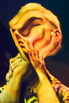 Distorted reflection of anxious young man touching head and screaming on dichroic film