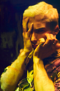 Distorted reflection of anxious young man touching head and screaming on dichroic film