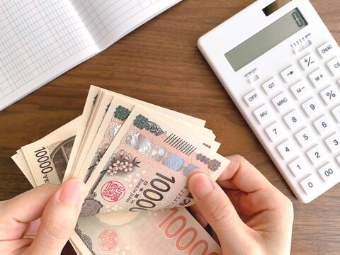 お金を数える女性の手と机上の白い電卓