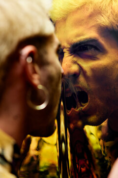 Enraged young male with earring yelling in dissatisfaction at reflection on dichroic film