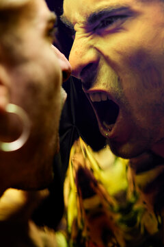 Enraged young male with earring yelling in dissatisfaction at reflection on dichroic film