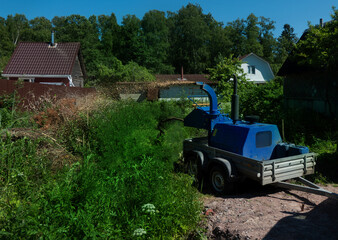 Male Arborist using a working wood chipper machine.The tree surgeon is wearing a safety helmet with a visor and ear protectors.