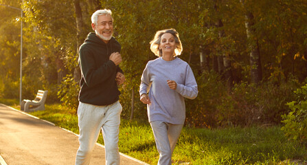 Energize your morning. Active mature family couple in sportswear running together in park on sunny...