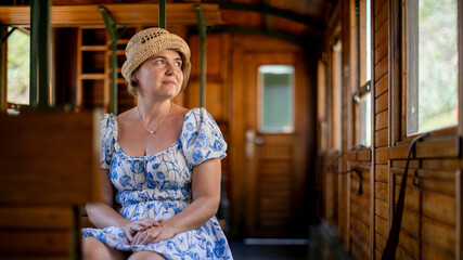 Spectacled Caucasian woman in vintage dress journeys on rustic train, evoking nostalgia, contemplative solitude, and Railway Heritage Day  Šarganska (sharganska) osmica