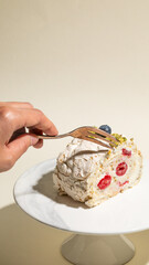A slice of raspberry-studded meringue roulade, poised for savoring by a hand, whispers flavors of...