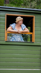 A contemplative Caucasian woman in vintage attire gazes from a rustic train, evoking Retro...