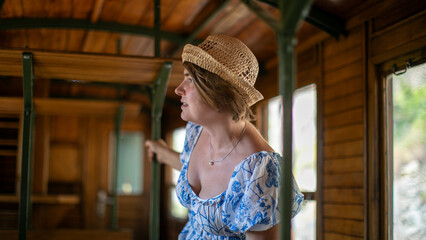 A Caucasian woman in a vintage train carriage, straw hat poised for adventure, embraces Wanderlust Day with nostalgic charm  Šarganska (sharganska) osmica