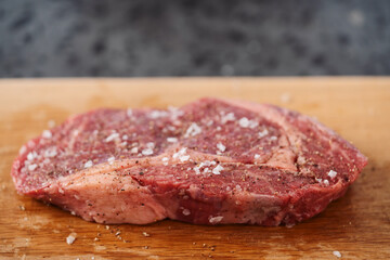 Raw ribeye steak spiced and ready to cook on oak board