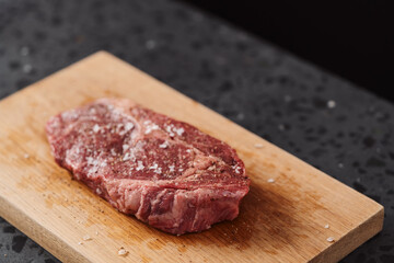 Raw ribeye steak spiced and ready to cook on oak board