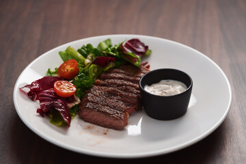 ribeye steak with garlic sauce and fresh salad on white plate on walnut table