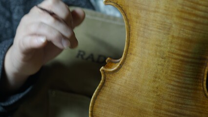 Skilled luthier applying protective varnish layer, hand crafting vintage style violin with meticulous antiquing techniques, creating rich patina and classic instrument aesthetic