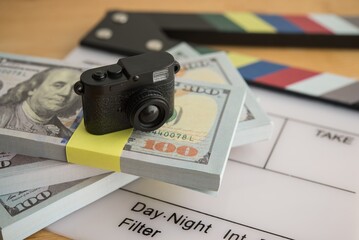 Digital camera on stack US dollar bill banknotes and clapperboard. Sell content photo or video clips and making money in stock photo microstock online website or mobile app, passive income concept.