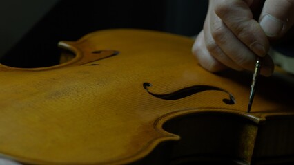 Luthier carefully applying dark varnish to handcrafted violin with soft brush, creating vintage...